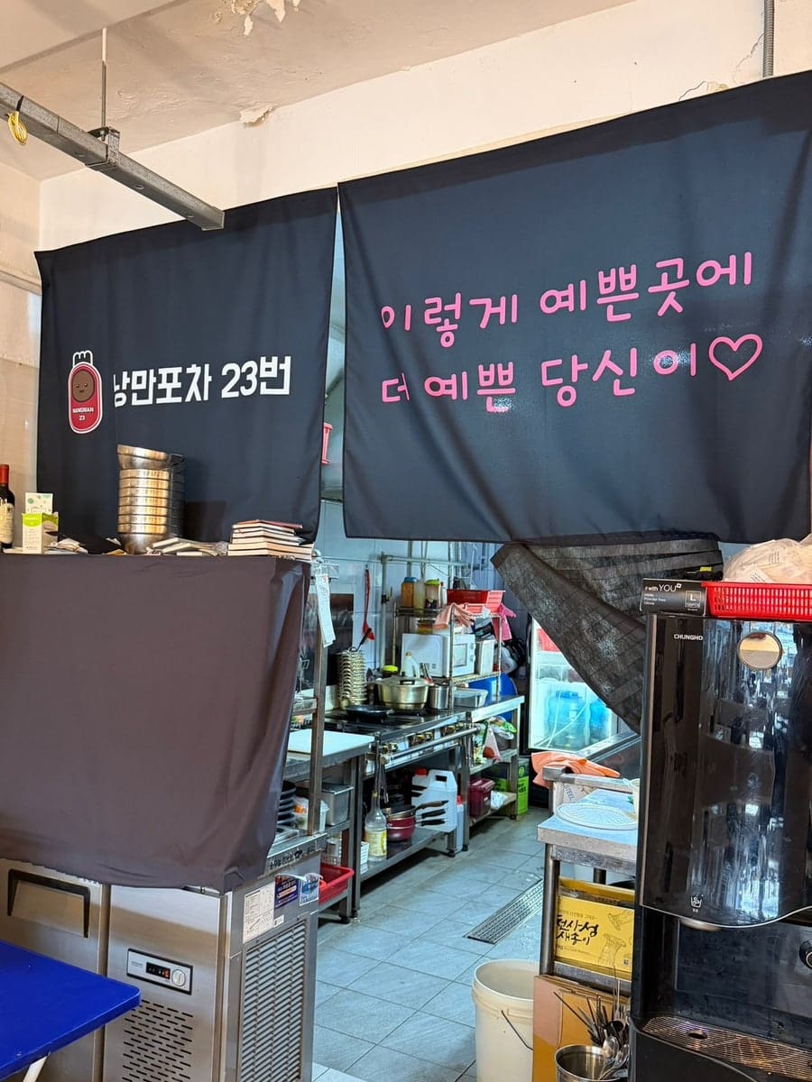 filly777이 담은 창가 자리와 실내 풍경입니다. 줄전구 너머로 케이블카 선로와 항구가 펼쳐지고, 벽걸이 TV와 선반 위 술병들이 힙한 인테리어를 보여줍니다.