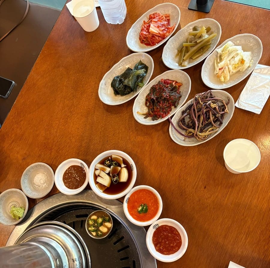 junotes는 고기만 덜렁 나오는 느낌이 아니라 여러 가지 반찬이 함께 차려져 한정식처럼 상이 꽉 찬다고 적었습니다. 나물과 김치 반찬이 접시마다 놓인 테이블과,