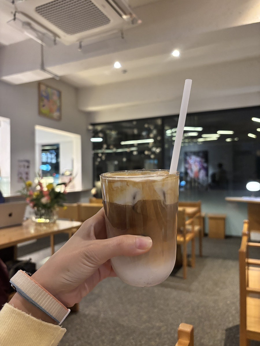 askuzk와 twinkling_j가 담은 장면입니다. 큰 통창 앞 우드 테이블에 앉아 거리를 내다보는 자리가 있고,